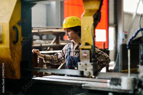 Worker operating industrial equipment in warehouse while wearing safety helmet and checked shirt