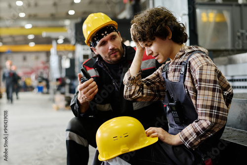 Two workers in workshop wearing hard hats engaging in conversation. Focus on person receiving guidance