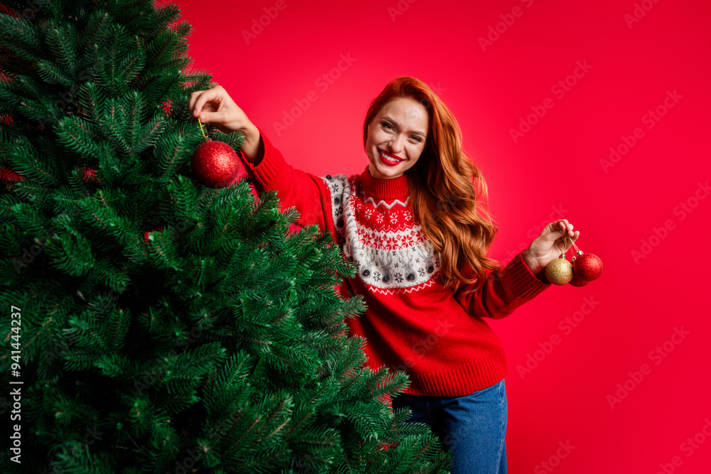 Photo of foxy young girl wearing ugly sweater decorating new year fir tree with baubles waiting for miracle isolated on red color background Photo of foxy young girl wearing ugly sweater decorating new year fir tree with baubles waiting for miracle isolated on red color background