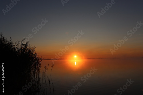 photo of a bright sunrise on a lake with haze