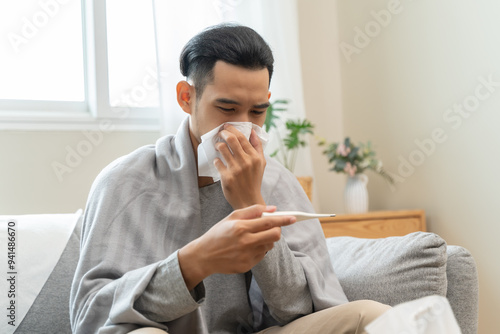 Seasonal cold sickness in people concept, Sick asian man looking at thermometer during measuring his body temperature feel exhausted and headache from fever.