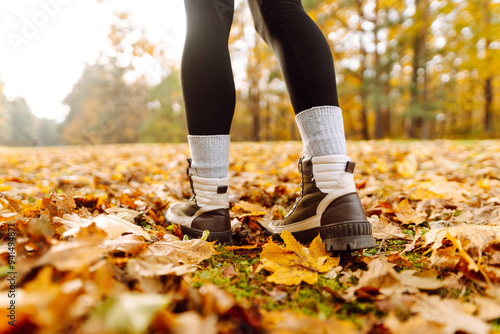 Close up of boots. A person strolls along a path blanketed with vibrant autumn leaves, enjoying a sunny day in a picturesque natural setting surrounded by trees. Healthy lifestyle on leisure activity.