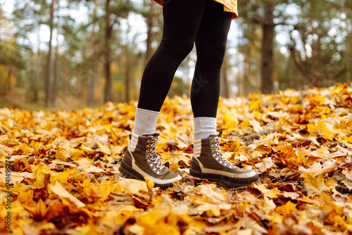 Close up of boots. A person strolls along a path blanketed with vibrant autumn leaves, enjoying a sunny day in a picturesque natural setting surrounded by trees. Healthy lifestyle on leisure activity.