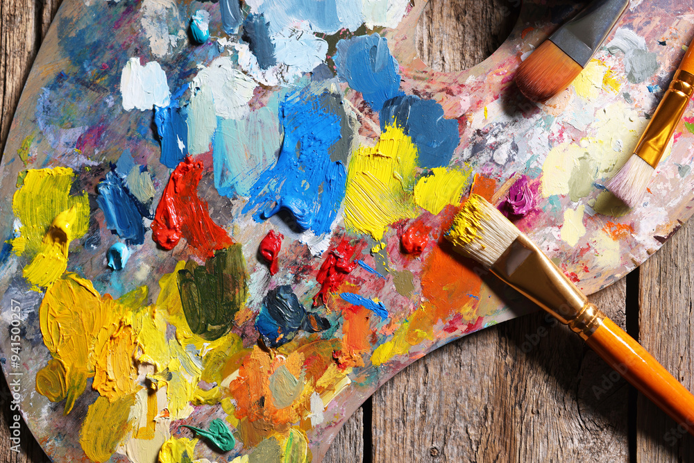 Fototapeta premium Artist's palette, brushes and paints on wooden table, flat lay