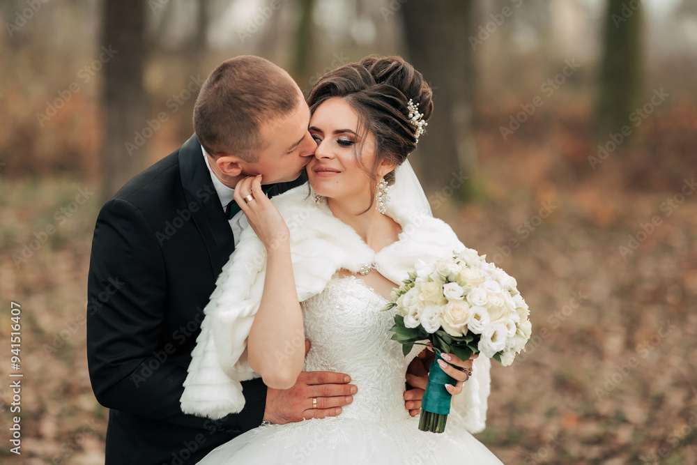 A bride and groom are hugging in the woods. The bride is wearing a white dress and a fur stole. The bride is holding a bouquet of flowers A bride and groom are hugging in the woods. The bride is wearing a white dress and a fur stole. The bride is holding a bouquet of flowers