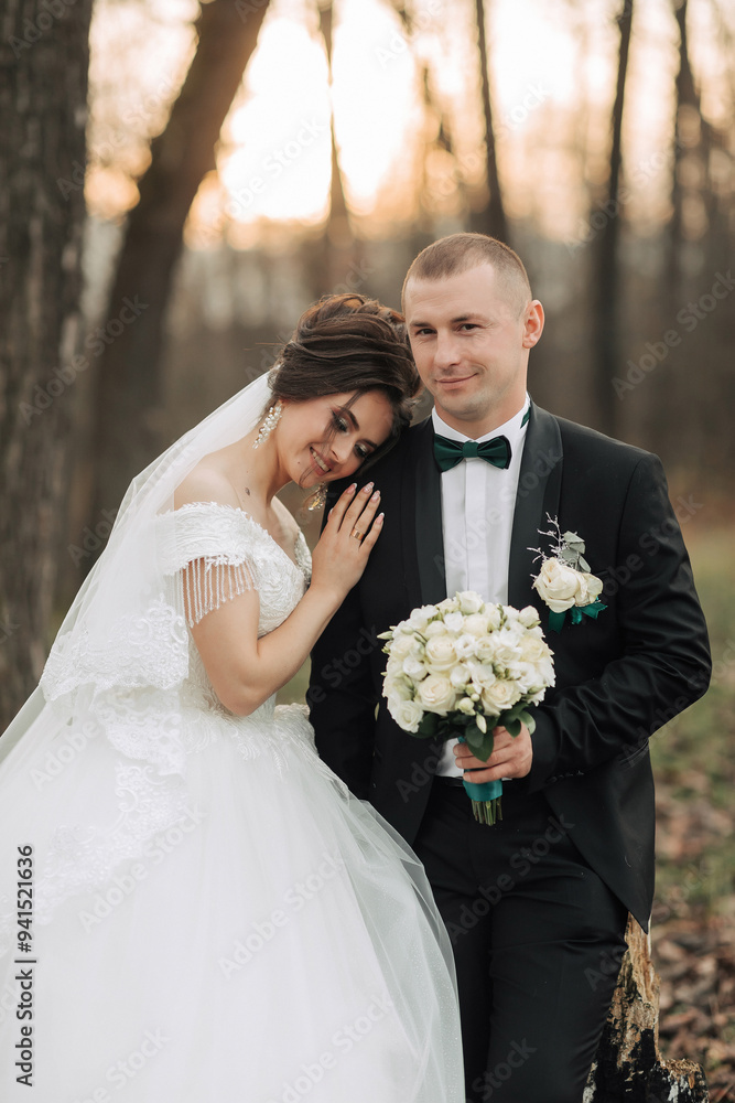 A bride and groom are posing for a picture in a forest. The bride is wearing a white dress and the groom is wearing a black suit. They are holding a bouquet and a bouquet of flowers A bride and groom are posing for a picture in a forest. The bride is wearing a white dress and the groom is wearing a black suit. They are holding a bouquet and a bouquet of flowers