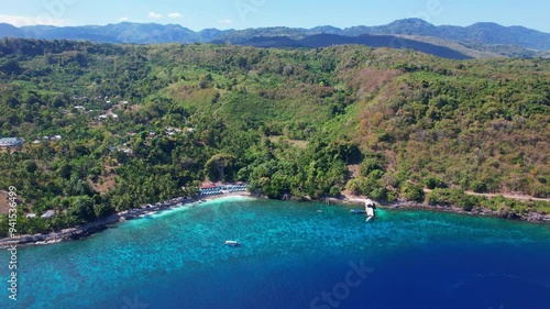 Aerial drone shot of a beautiful local market in Lola, Alor regency, Indonesia. The view shows the surrounding of all the green mountains around, contrasted with the strong blue and clear water color.