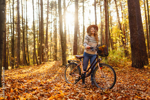 Young woman enjoys a sunny autumn day while riding her bicycle through a forest filled with colorful fallen leaves. Active lifestyle.