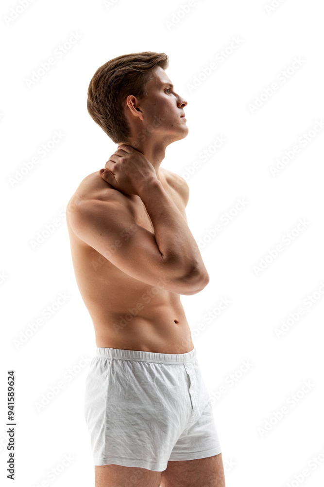 Side view photo of young athletic man touches back of his neck, as if he feel pain in muscles against white studio background. Concept of male health, natural beauty people, fashion, self care. Side view photo of young athletic man touches back of his neck, as if he feel pain in muscles against white studio background. Concept of male health, natural beauty people, fashion, self care.