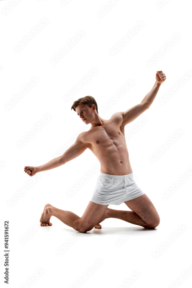 Fototapeta premium Dynamic photo of young man in white boxers, underwear posing, kneels with arms raised against white studio background. Concept of male health, natural beauty people, fashion, self care.