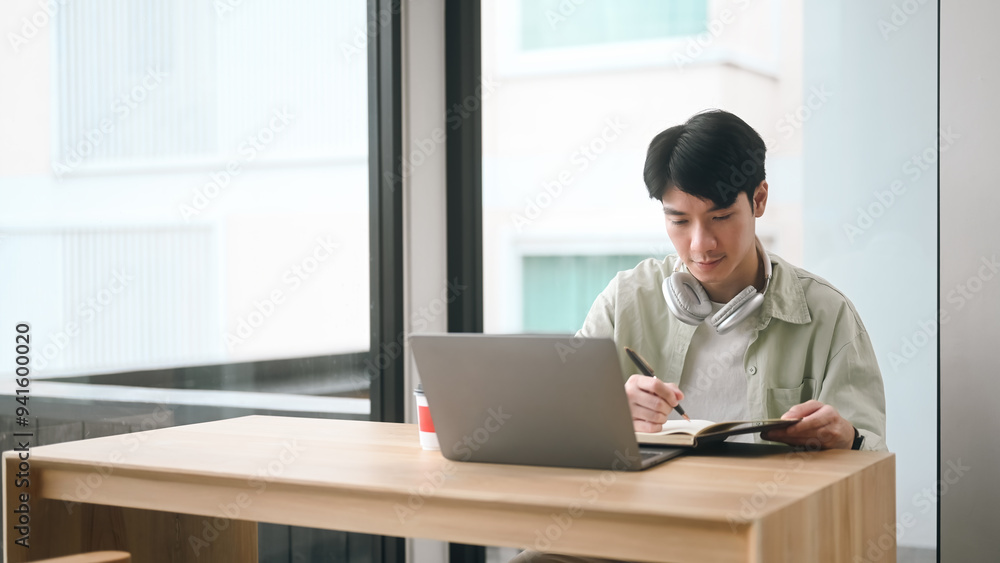 A man is sitting at a table with a laptop and a notebook A man is sitting at a table with a laptop and a notebook