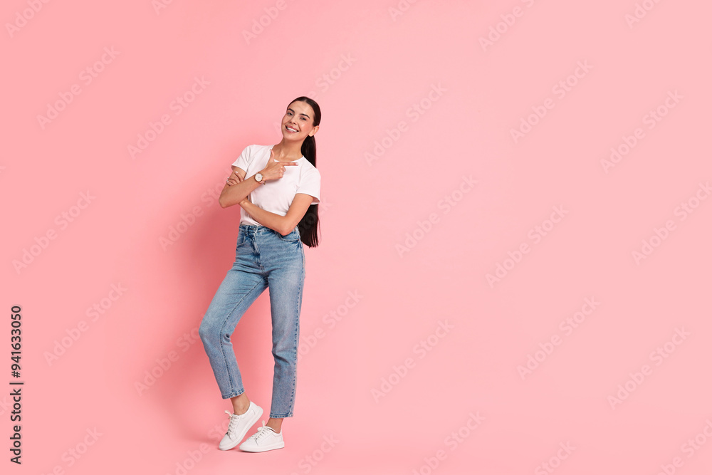 Smiling woman pointing at something on pink background. Space for text Smiling woman pointing at something on pink background. Space for text