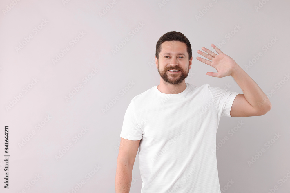 Cheerful man waving on light background. Space for text Cheerful man waving on light background. Space for text