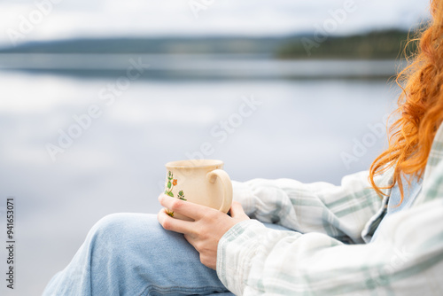 Person holding a mug by a serene lake during camping photo