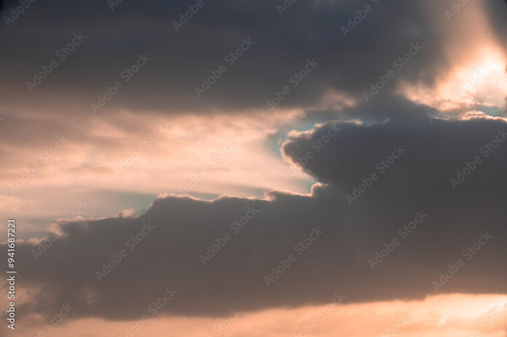 Obraz premium The sky is filled with clouds and the sun is setting. The clouds are dark and the sky is a mix of orange and blue
