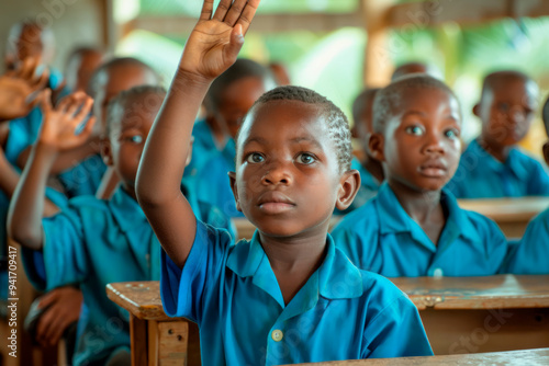 African children in blue uniforms sit at desks in a classroom in an African rural primary school, raising their hands to answer or ask a question to the teacher