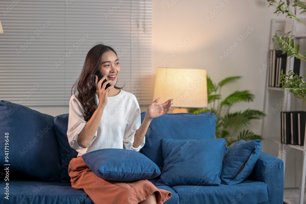 Young woman sitting on sofa talking on mobile phone at night at home Young woman sitting on sofa talking on mobile phone at night at home