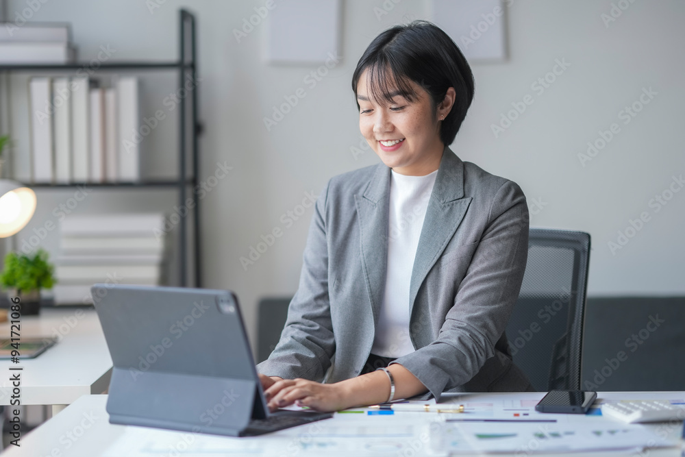 Young asian businesswoman smiling and working on tablet at her desk in office Young asian businesswoman smiling and working on tablet at her desk in office