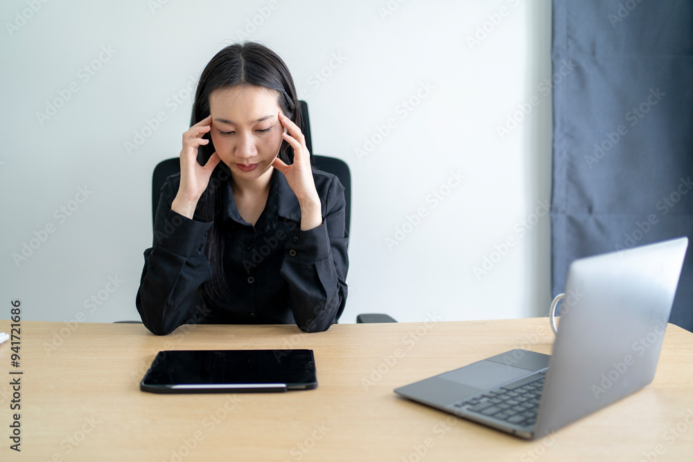 Stressed asian businesswoman suffering from headache while working on laptop in office Stressed asian businesswoman suffering from headache while working on laptop in office