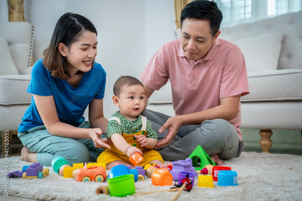 A family of three, a man and two women, are playing with toys on the floor. The baby is holding a toy truck and the parents are clapping. Scene is happy and playful A family of three, a man and two women, are playing with toys on the floor. The baby is holding a toy truck and the parents are clapping. Scene is happy and playful