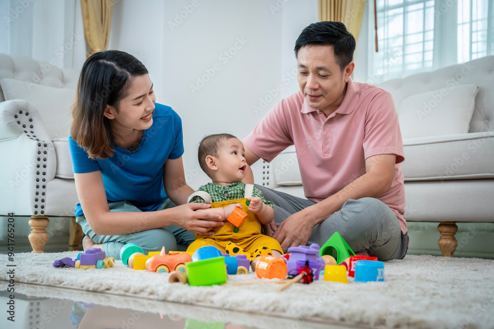 A family of three, a man and two women, are playing with toys on the floor. The baby is holding a toy truck and the parents are clapping. Scene is happy and playful A family of three, a man and two women, are playing with toys on the floor. The baby is holding a toy truck and the parents are clapping. Scene is happy and playful