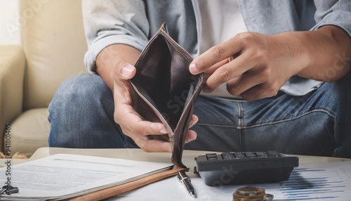 Facing a bankruptcy crisis, a young man opens his empty wallet in distress, struggling to find money to pay off his mortgage debt.
