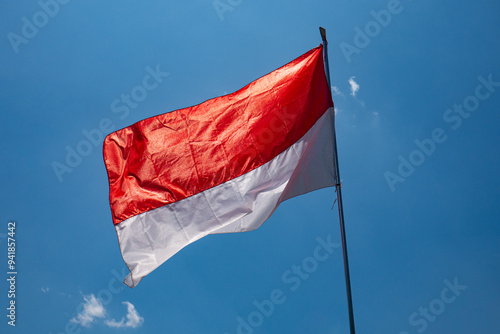 close up of the Indonesian red and white flag fluttering in the wind, with a blue sky and sunlight in the background.
