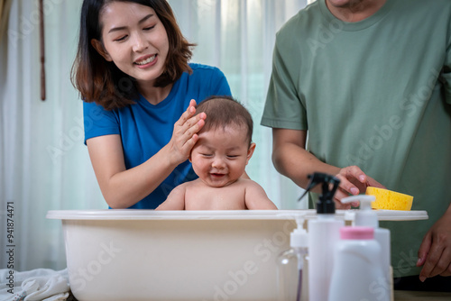 The father and mother are helping each other bathe their baby in a bathtub. In the picture, everyone looks happy.