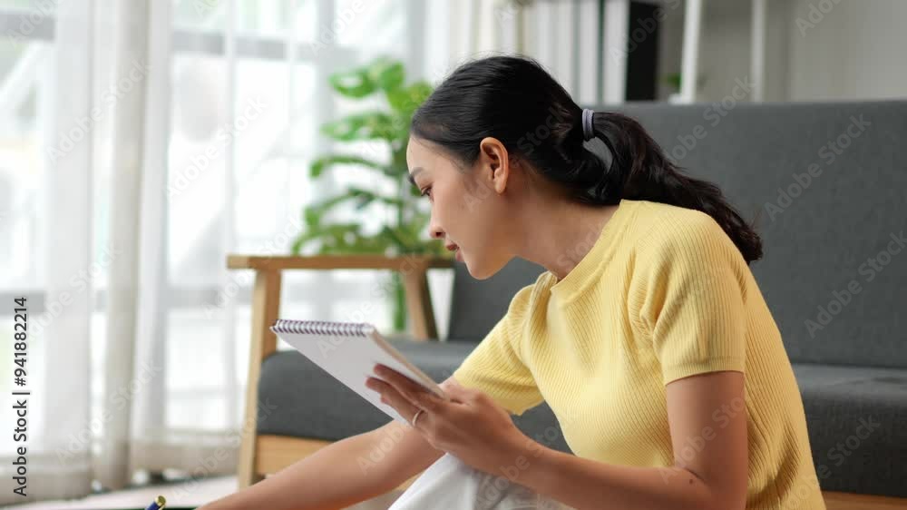 Thoughtful young woman jotting down notes while seated on the living room floor Thoughtful young woman jotting down notes while seated on the living room floor