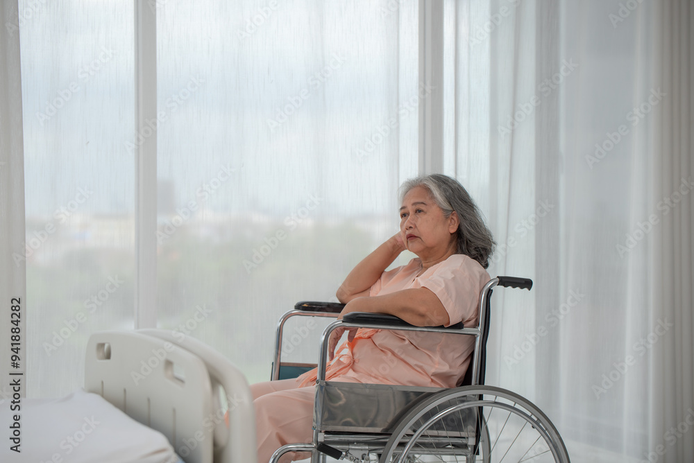 Depressed senior Asian woman patient in hospital sitting in wheelchair by the window, upset disabled patient thinking and looking out window, feeling lonely, nostalgia and melancholy Depressed senior Asian woman patient in hospital sitting in wheelchair by the window, upset disabled patient thinking and looking out window, feeling lonely, nostalgia and melancholy