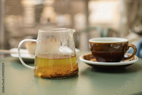 A glass teapot with buckwheat tea and a ceramic cup on the table on the summer terrace.