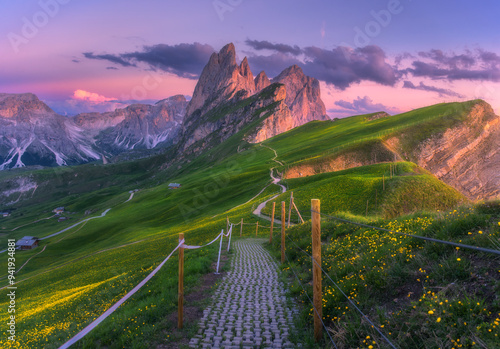 Seceda mountain at beautiful sunset in summer in Dolomites, Italy. Colorful landscape with mountain peaks, rocks, alpine meadows, trail, green grass, purple sky at dusk. Hiking in Alps. Landscape photo