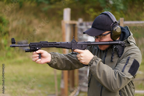 A man is holding a gun and wearing a green jacket. He is wearing a black hat and glasses