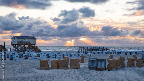 Strandkörbe und Pfahlbauten am Strand von Sankt Peter-Ording vor dramatischem Himmel am Abend photo