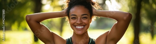 A young woman smiles brightly outdoors, with her hands behind her head, showcasing a joyful and confident expression surrounded by greenery