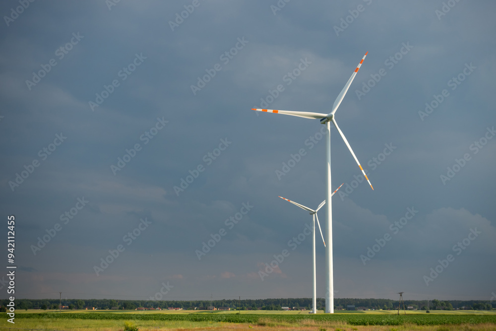 Distant white wind turbines against a dramatic cloudy sky. Meadow in the foreground, taken late afternoon
