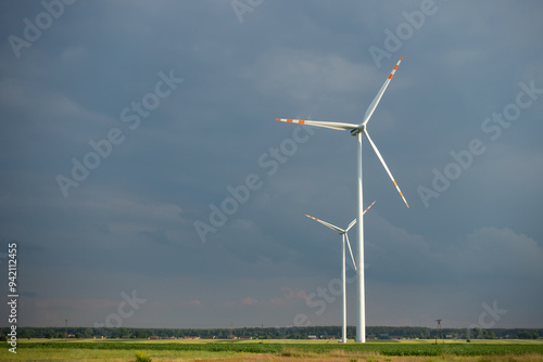 Obraz na płótnie Distant white wind turbines against a dramatic cloudy sky. Meadow in the foreground, taken late afternoon w salonie