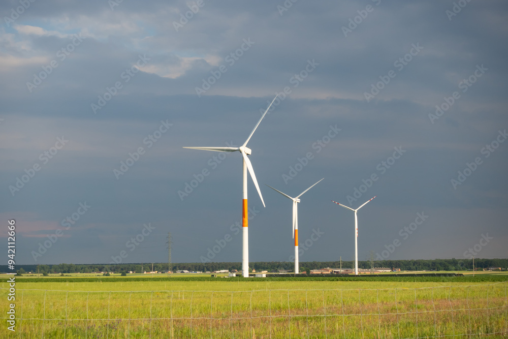 Distant white wind turbines against a dramatic cloudy sky. Meadow in the foreground, taken late afternoon Distant white wind turbines against a dramatic cloudy sky. Meadow in the foreground, taken late afternoon