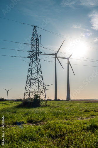 Obraz na płótnie Wind turbines and high voltage electric pylon against blue sky. Sun shining behind the turbines w salonie