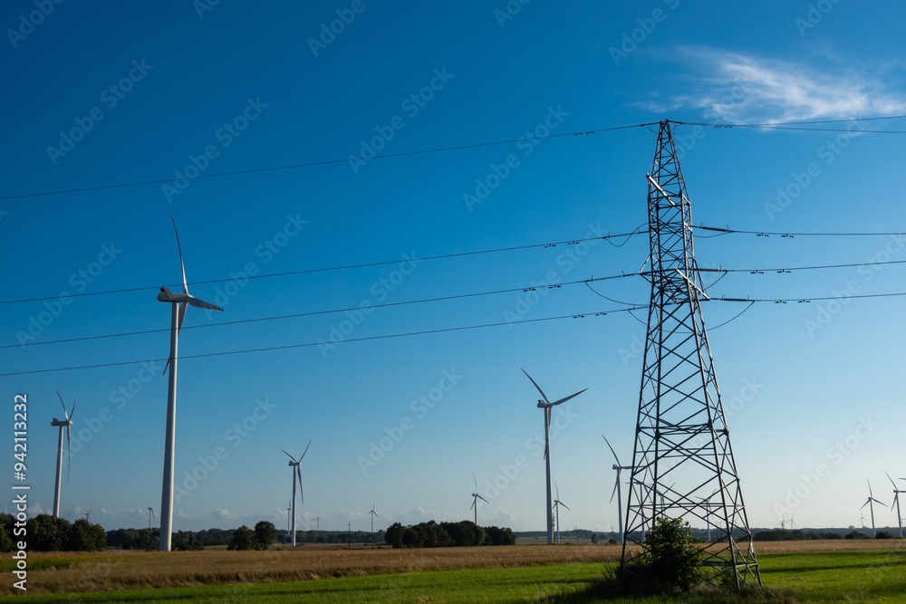 Wind turbines and high voltage electric pylon against blue sky. Sun shining behind the turbines