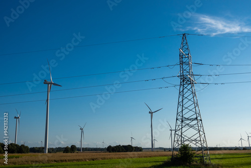 Obraz na płótnie Wind turbines and high voltage electric pylon against blue sky. Sun shining behind the turbines w salonie