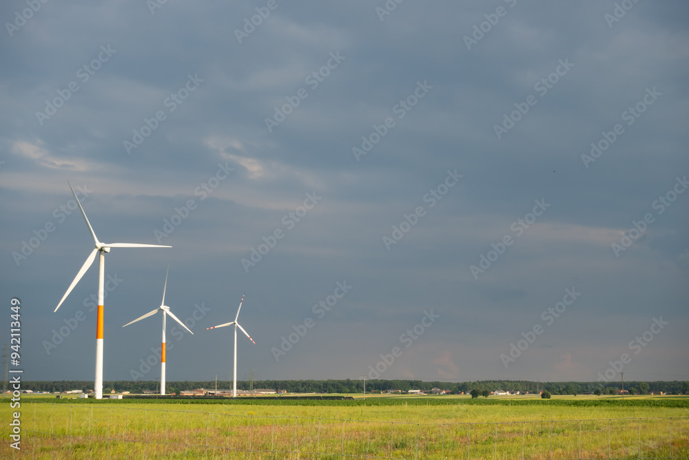 Distant white wind turbines against a dramatic cloudy sky. Meadow in the foreground, taken late afternoon