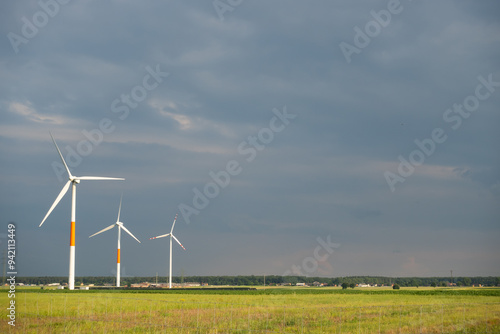Obraz na płótnie Distant white wind turbines against a dramatic cloudy sky. Meadow in the foreground, taken late afternoon w salonie