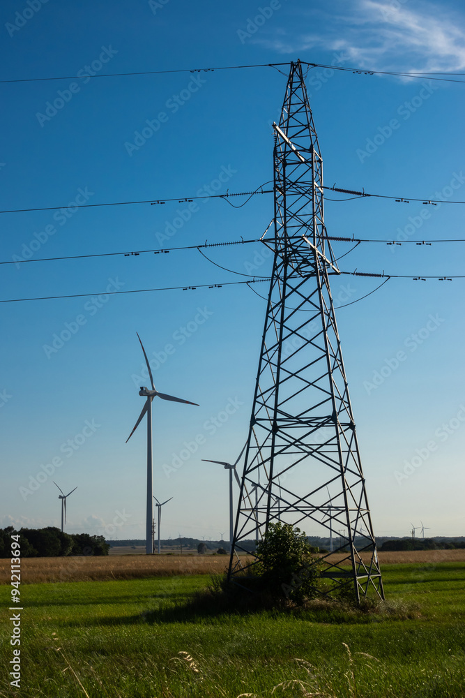 Wind turbines and high voltage electric pylon against blue sky. Sun shining behind the turbines