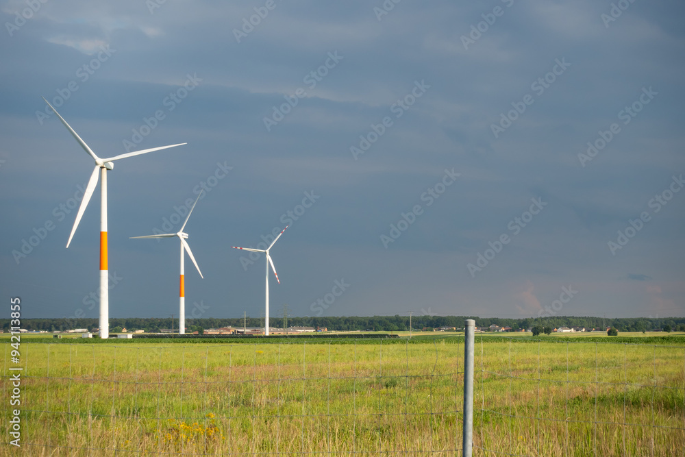 Distant white wind turbines against a dramatic cloudy sky. Meadow in the foreground, taken late afternoon