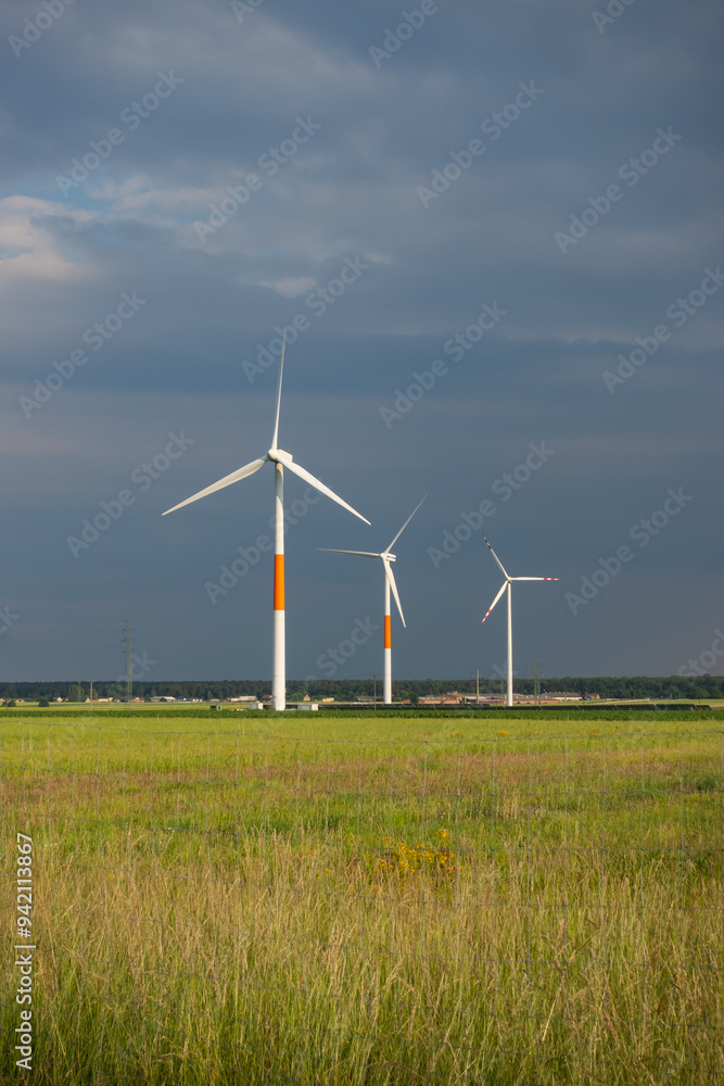 Distant white wind turbines against a dramatic cloudy sky. Meadow in the foreground, taken late afternoon