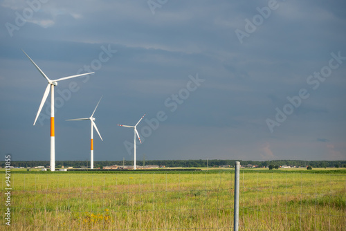 Obraz na płótnie Distant white wind turbines against a dramatic cloudy sky. Meadow in the foreground, taken late afternoon w salonie