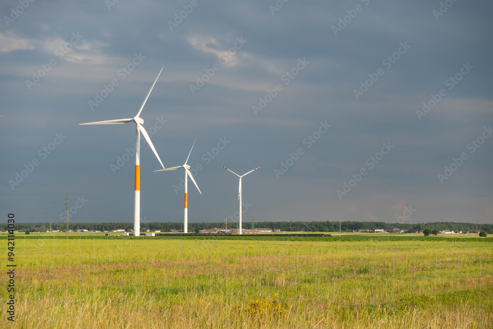 Distant white wind turbines against a dramatic cloudy sky. Meadow in the foreground, taken late afternoon