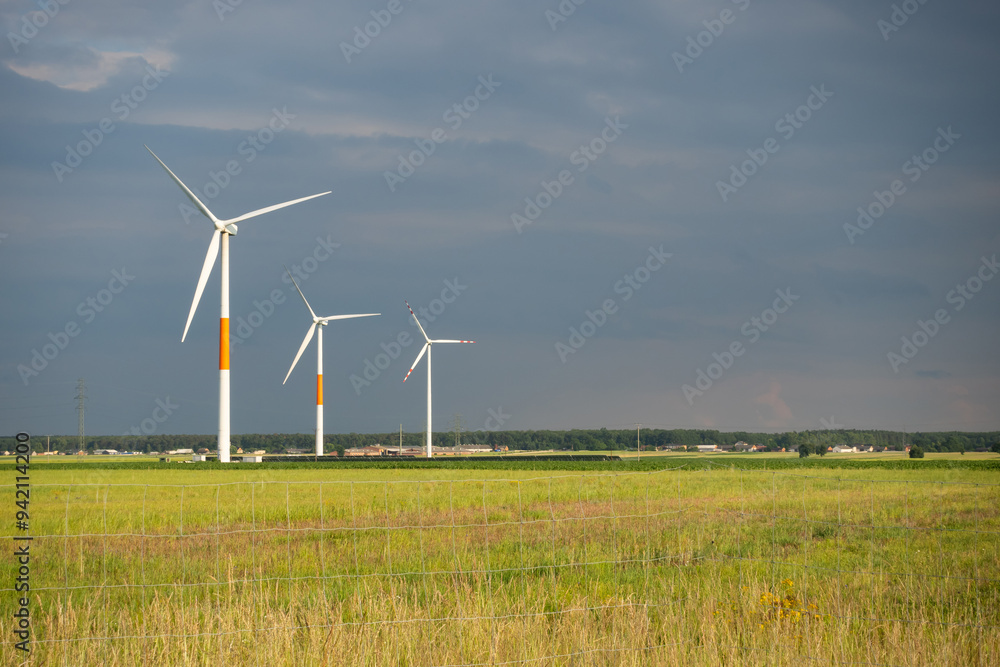 Distant white wind turbines against a dramatic cloudy sky. Meadow in the foreground, taken late afternoon
