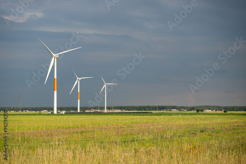 Obraz na płótnie Distant white wind turbines against a dramatic cloudy sky. Meadow in the foreground, taken late afternoon w salonie